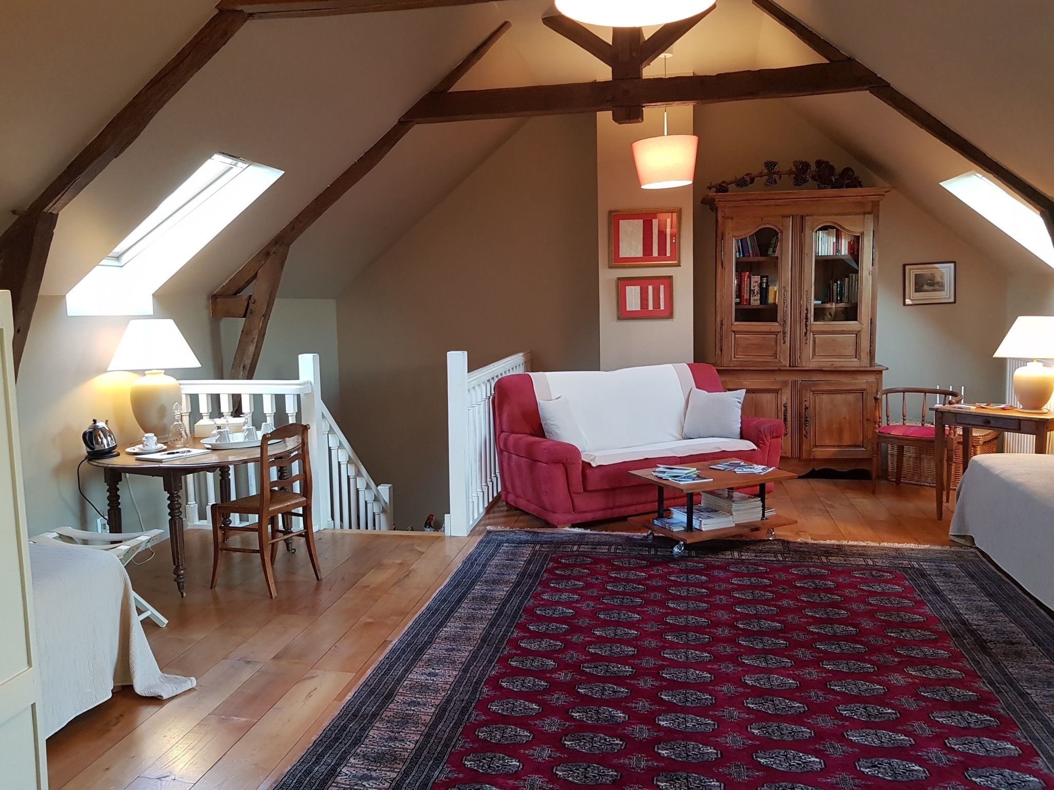 A cozy attic bedroom with a red sofa, wooden floor, and a large cabinet.
