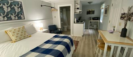 A hotel room with a bed, a desk, a chair, a kitchenette, and a bathroom.