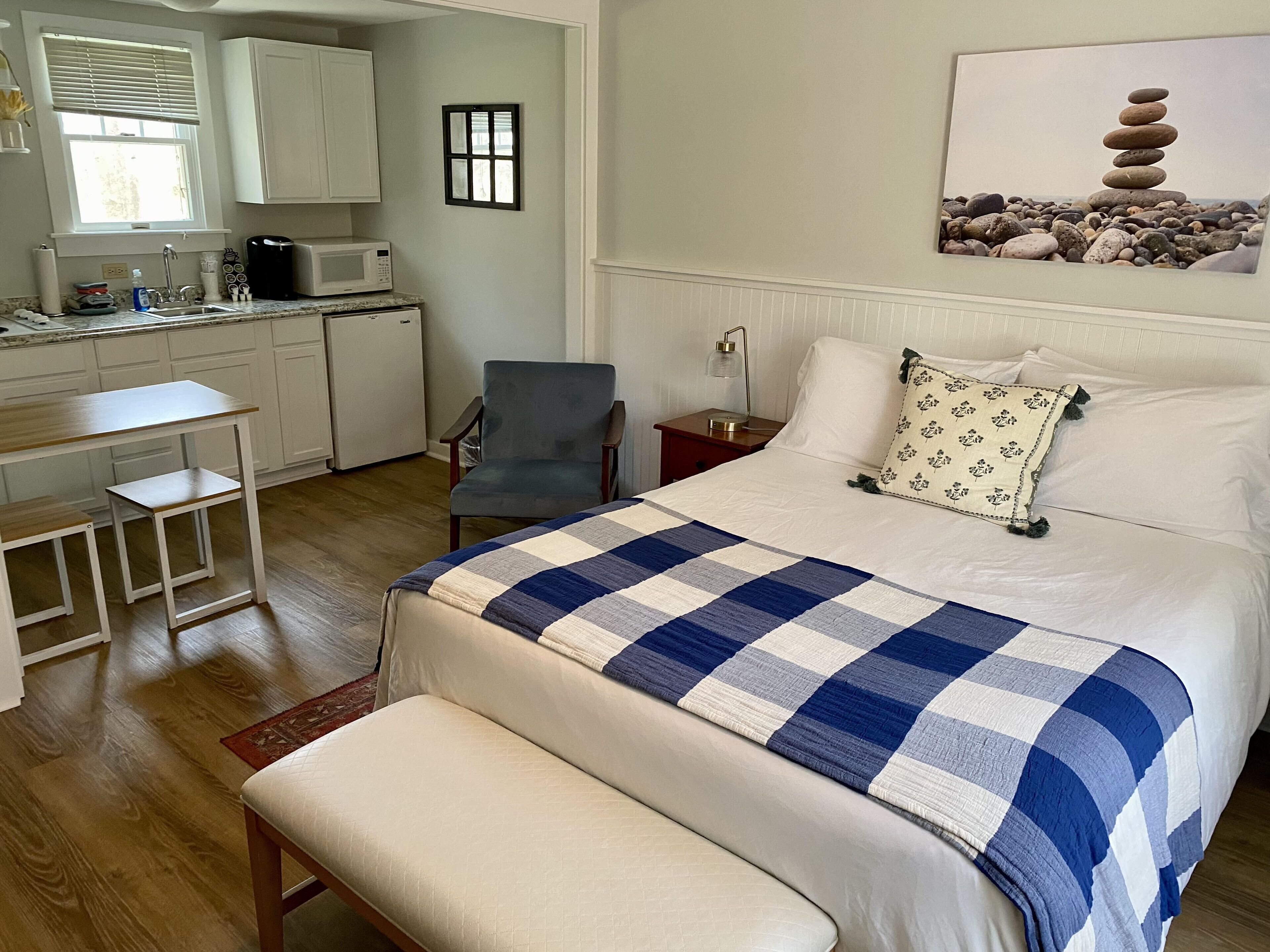 Une chambre à coucher avec un lit, un bureau, une chaise, une table de chevet et un tableau accroché au mur.