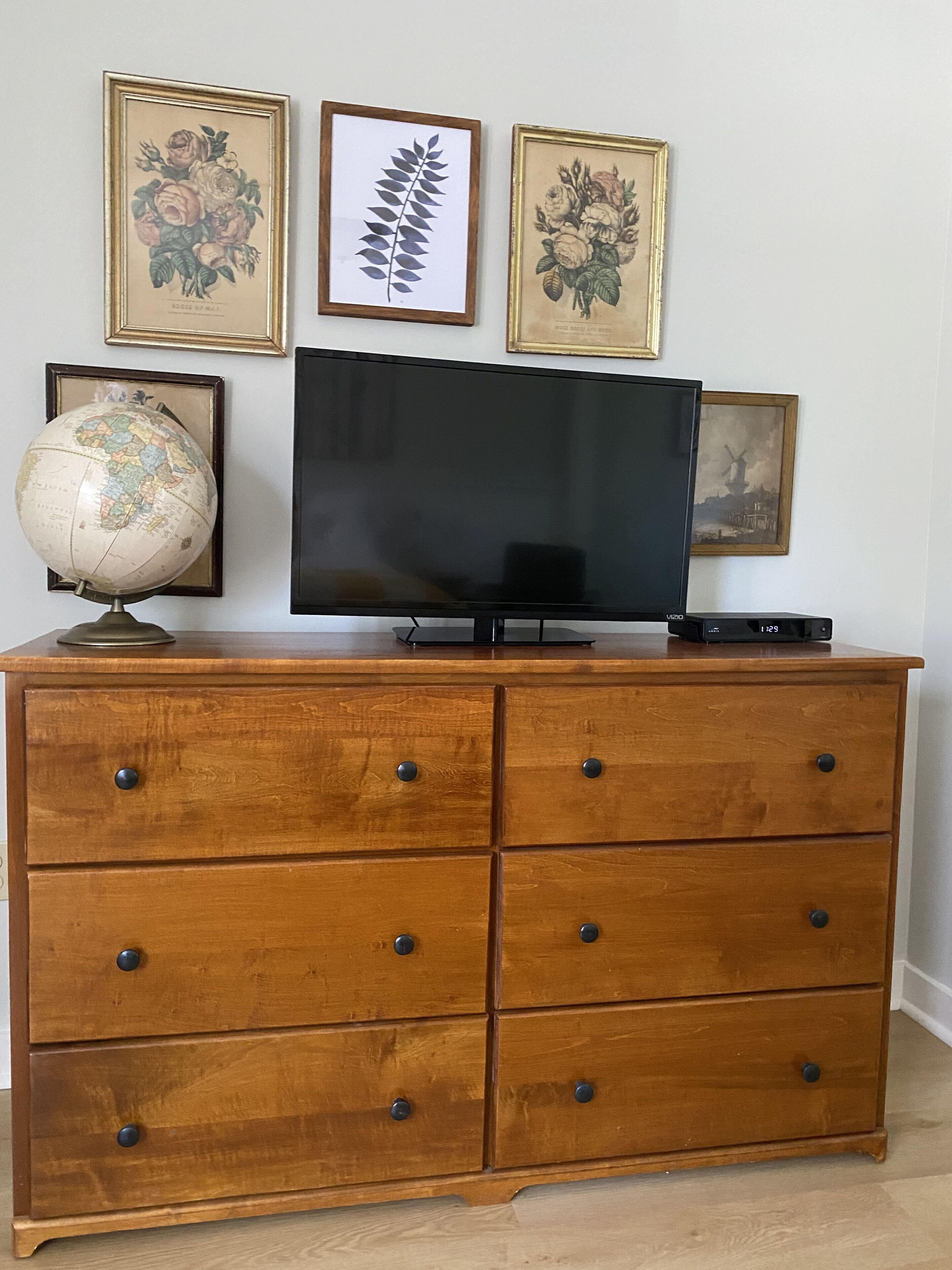 A wooden dresser with drawers, a globe, and a flat-screen TV on top.