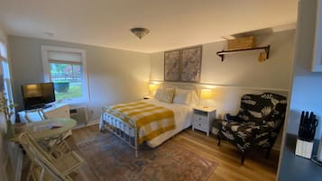 A bedroom with a bed, bedside tables, a chair, a desk, a television, and a window.