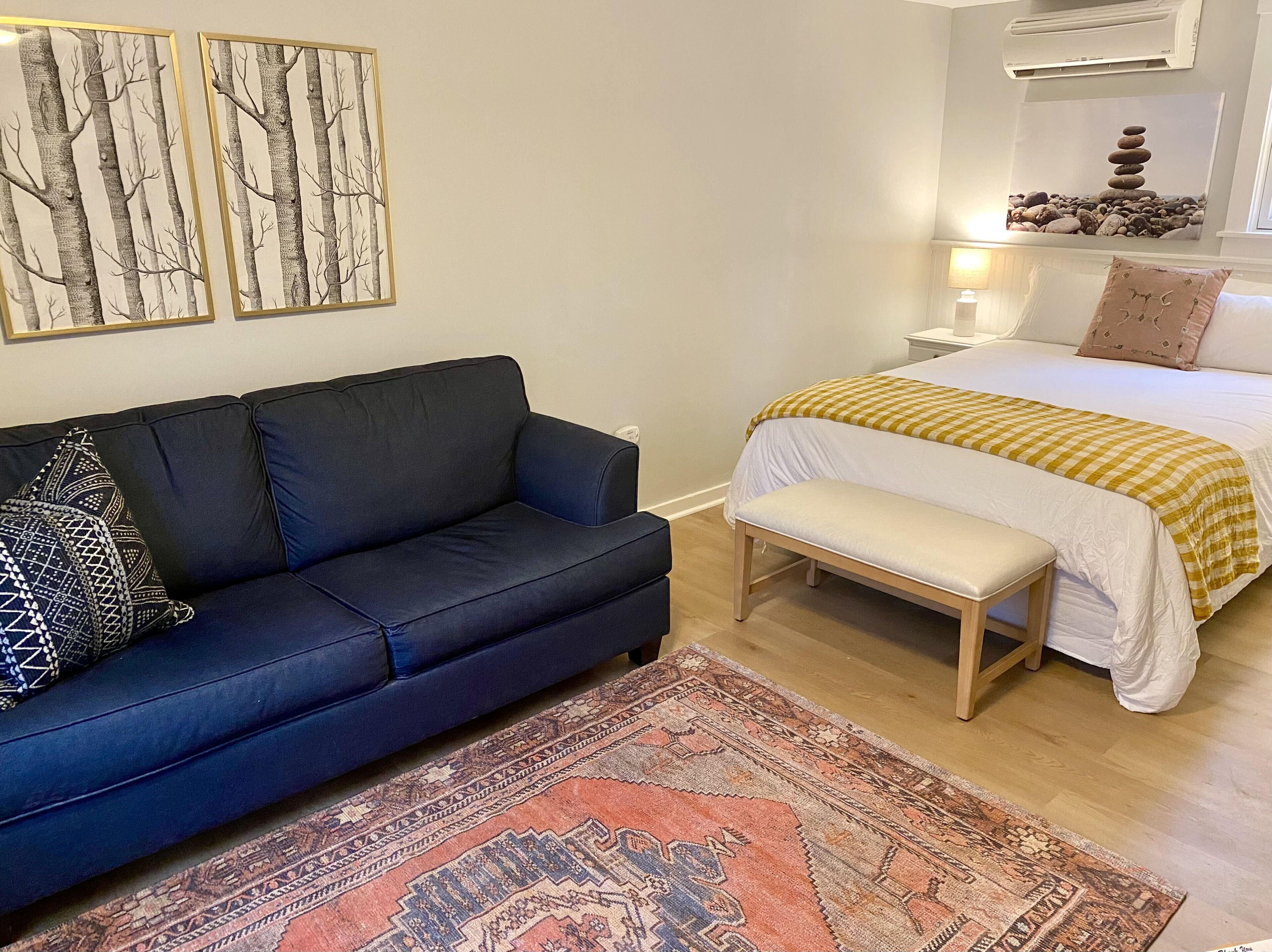 Ein Schlafzimmer mit Bett, Nachttisch, Lampe, einer Bank, einem Sofa und zwei Wandklimageräten.