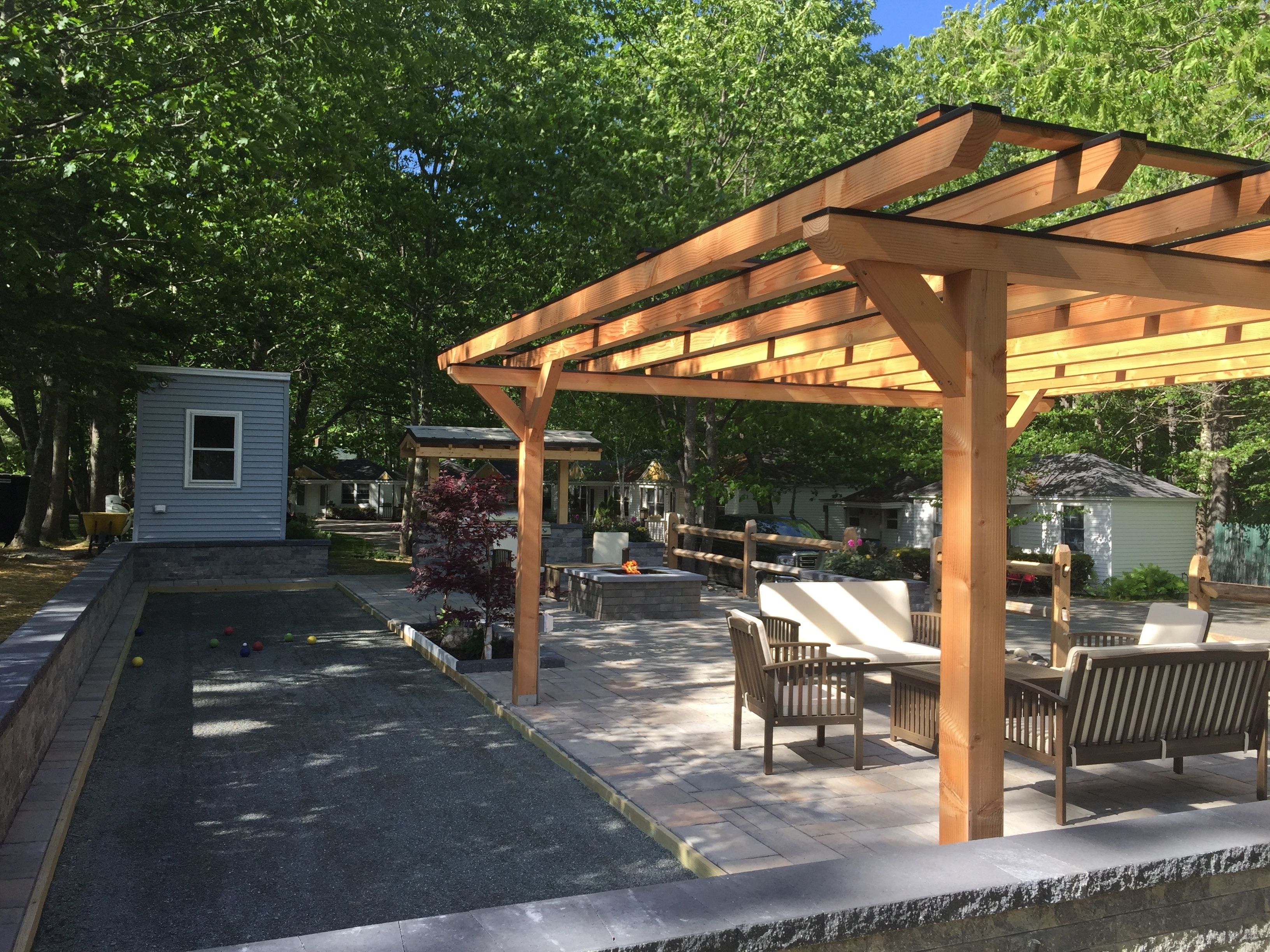 A wooden pergola structure with seating and a small shed in a residential outdoor area.