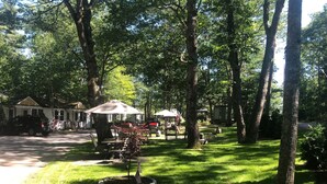 A park with picnic tables, a small tree with American flags, and a stone bench. - Hanscom's Motel and Cottages (Bar Harbor)
