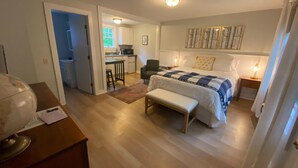 A bedroom with a bed, a bench, a desk, and a kitchenette in the background. - Hanscom's Motel and Cottages (Bar Harbor)