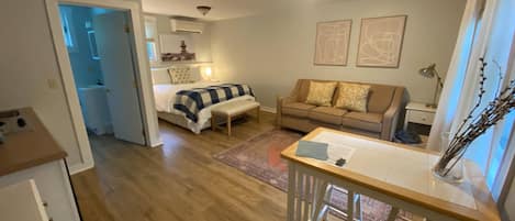 A cozy living room with a bed, a sofa, a dining table, and a kitchen area.
