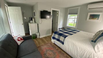 A bedroom with a bed, a sofa, a television, a window, and a door.
