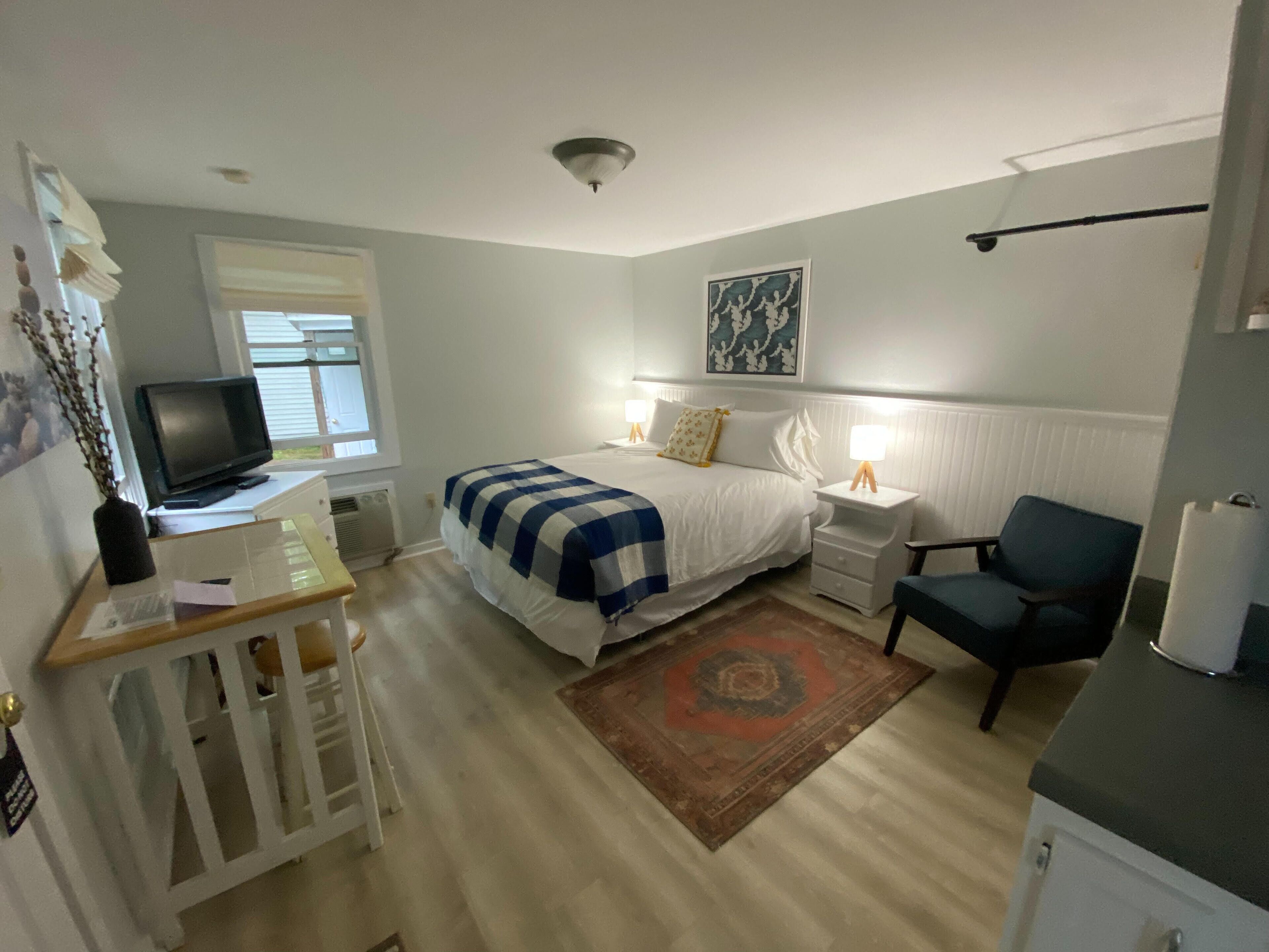 Een slaapkamer met een bed, nachtkastjes, een bureau, een stoel, een televisie en een raam.