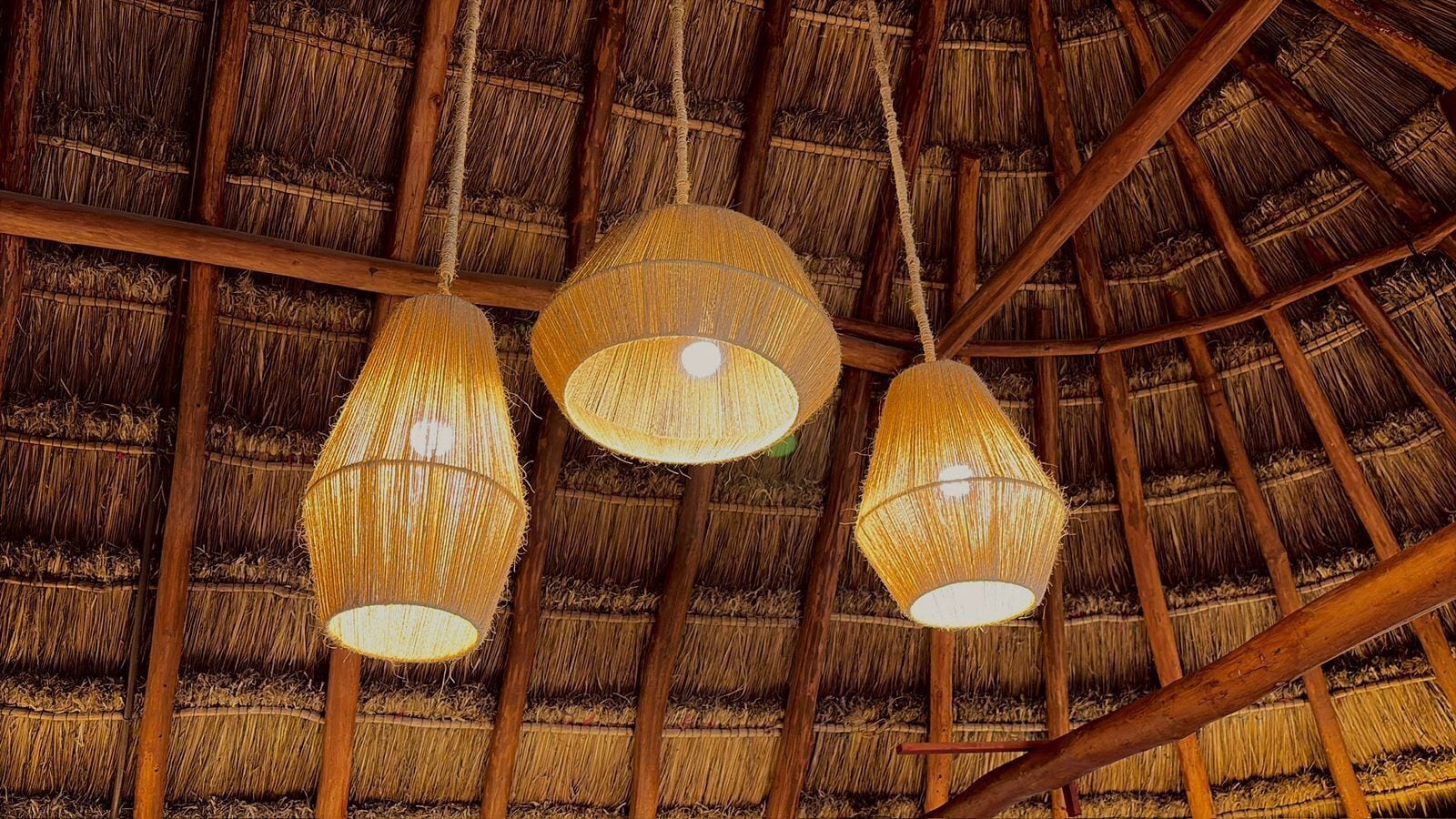 A thatched roof structure with three hanging woven light fixtures.