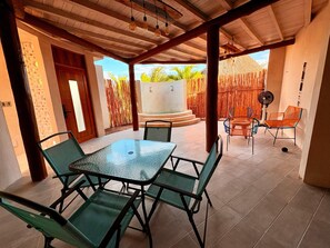 A covered patio area with a table and chairs, a fan, and a view of the outdoors.