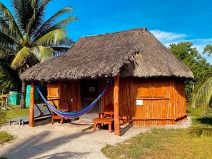 A thatched-roof hut with a hammock, wooden furniture, and a sandy ground.