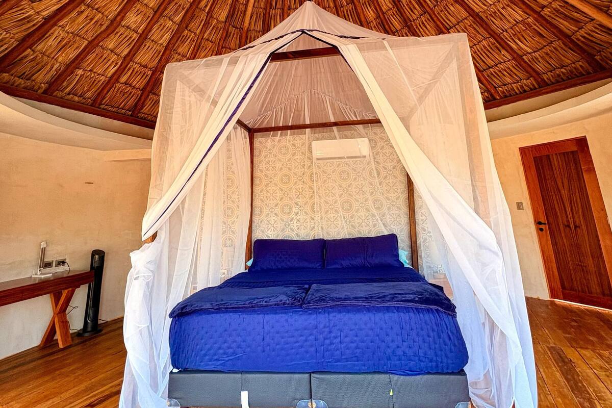 A room with a thatched ceiling, a bed with a canopy, and a wooden floor.