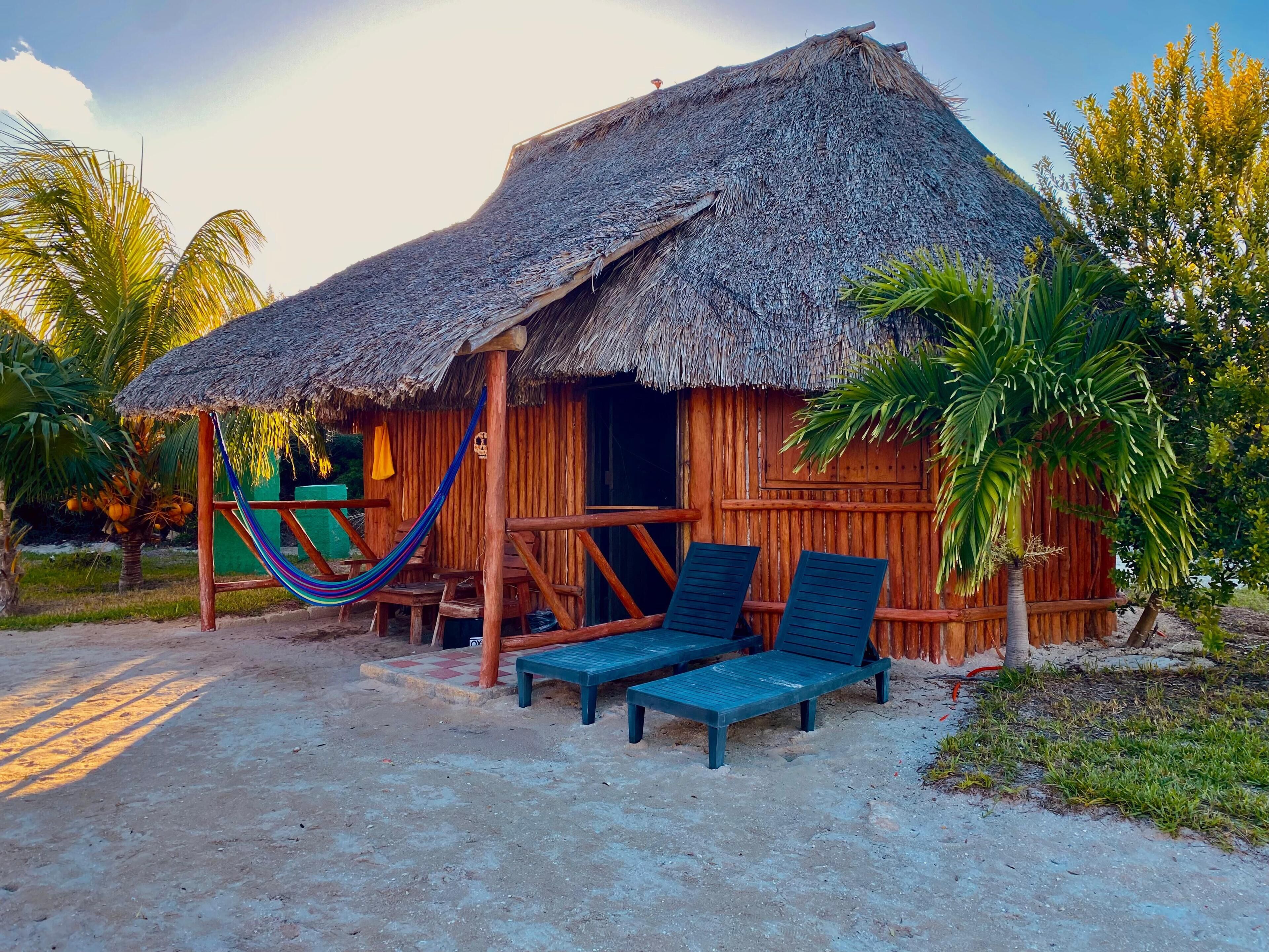 A thatched-roof hut with two lounge chairs and a hammock.