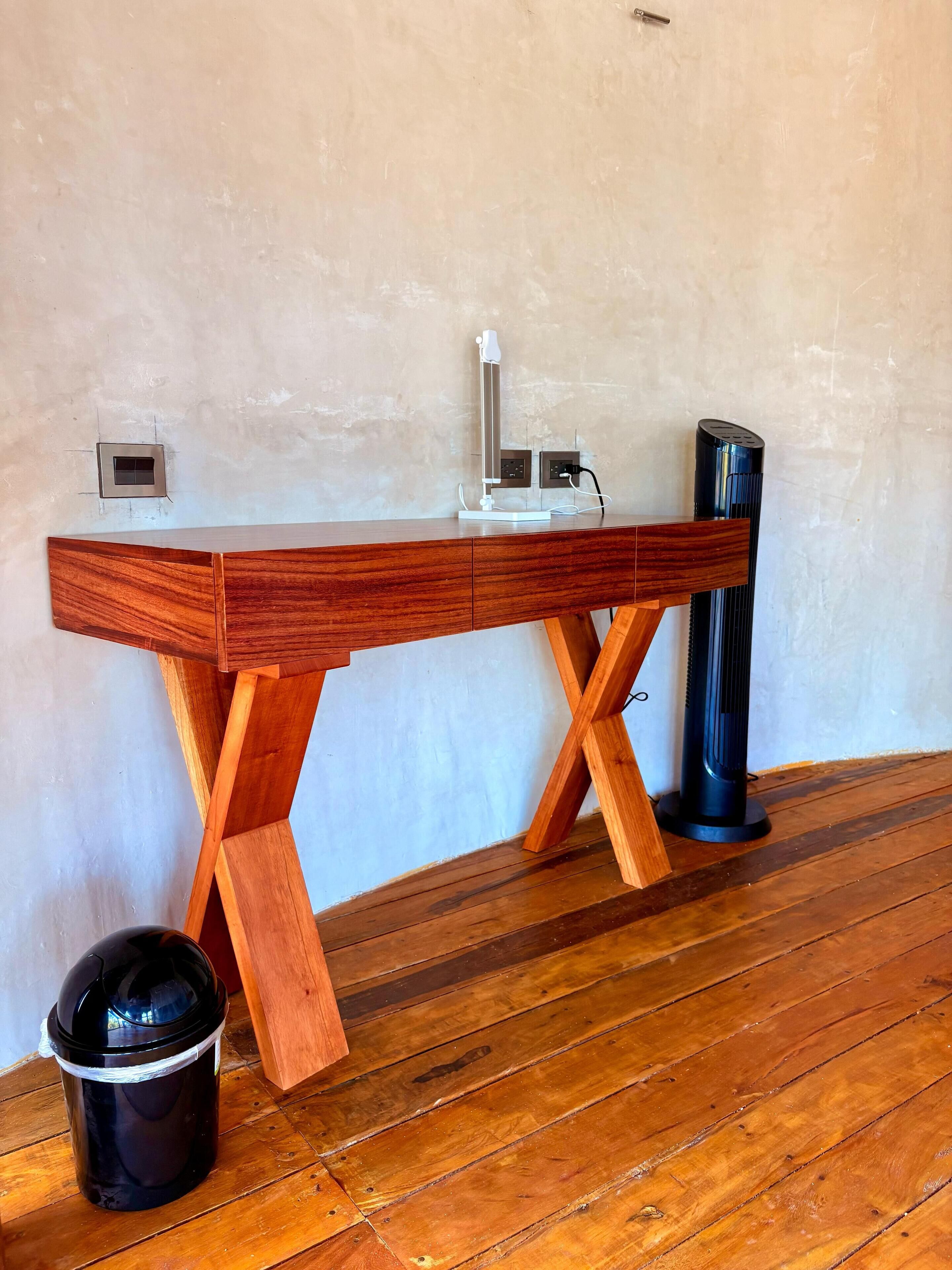 Un escritorio de madera con una lámpara moderna, un cubo de basura negro y un calentador vertical.