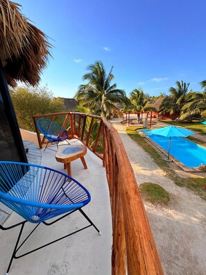 A poolside area with a wooden deck, a blue chair, a small table, and a thatched roof structure.