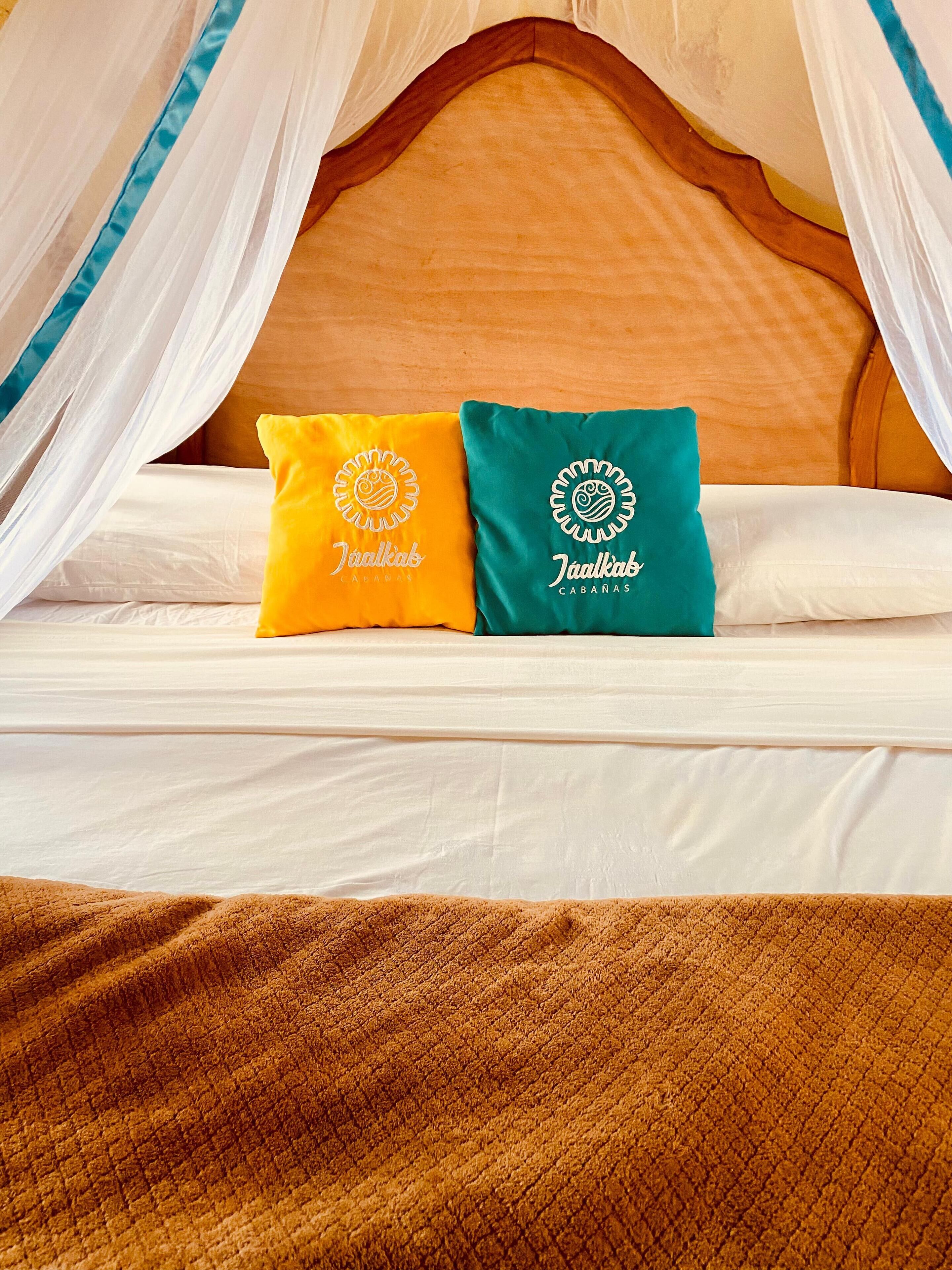 Una cama con dos almohadas, una amarilla y otra verde, con cabecera de madera y ropa de cama blanca.