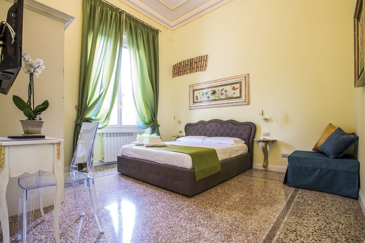 Un dormitorio con cama, escritorio, silla, planta en maceta y ventana con cortinas.