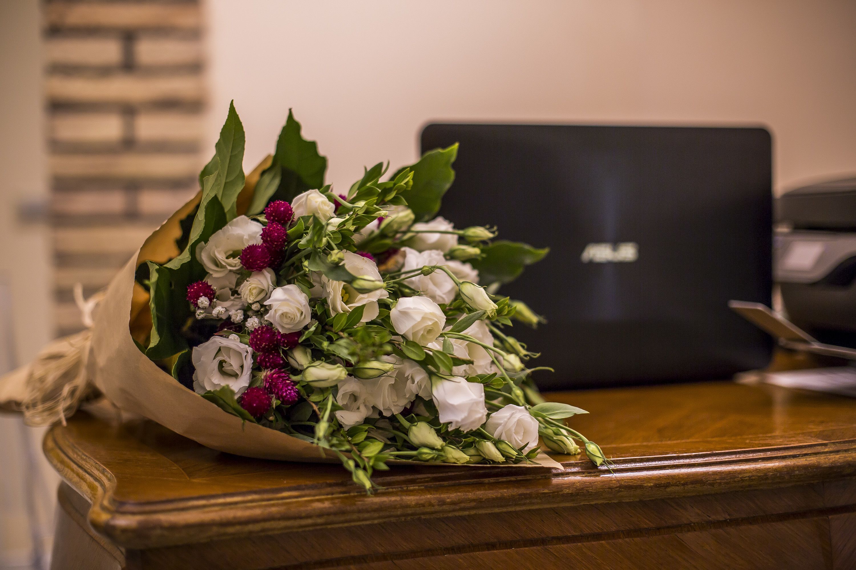 Un ramo de flores sobre una mesa de madera, con un ordenador portátil al fondo.