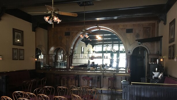 Interior de restaurante con asientos de bar, ventanas arqueadas y una barra.
