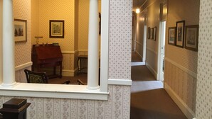 Un pasillo con papel tapiz estampado, cuadros enmarcados en las paredes y un piano al frente.