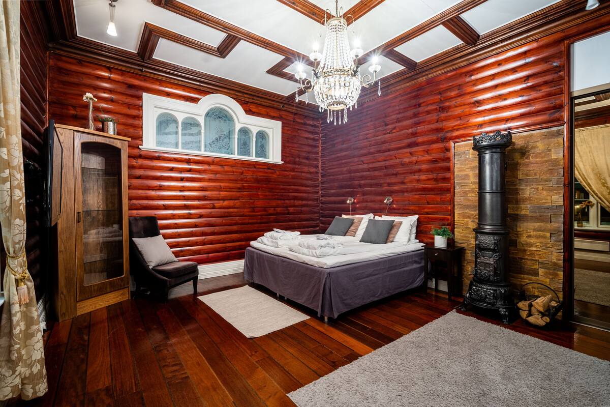 A log cabin bedroom with a bed, a chair, a dresser, a chandelier, and a fireplace.