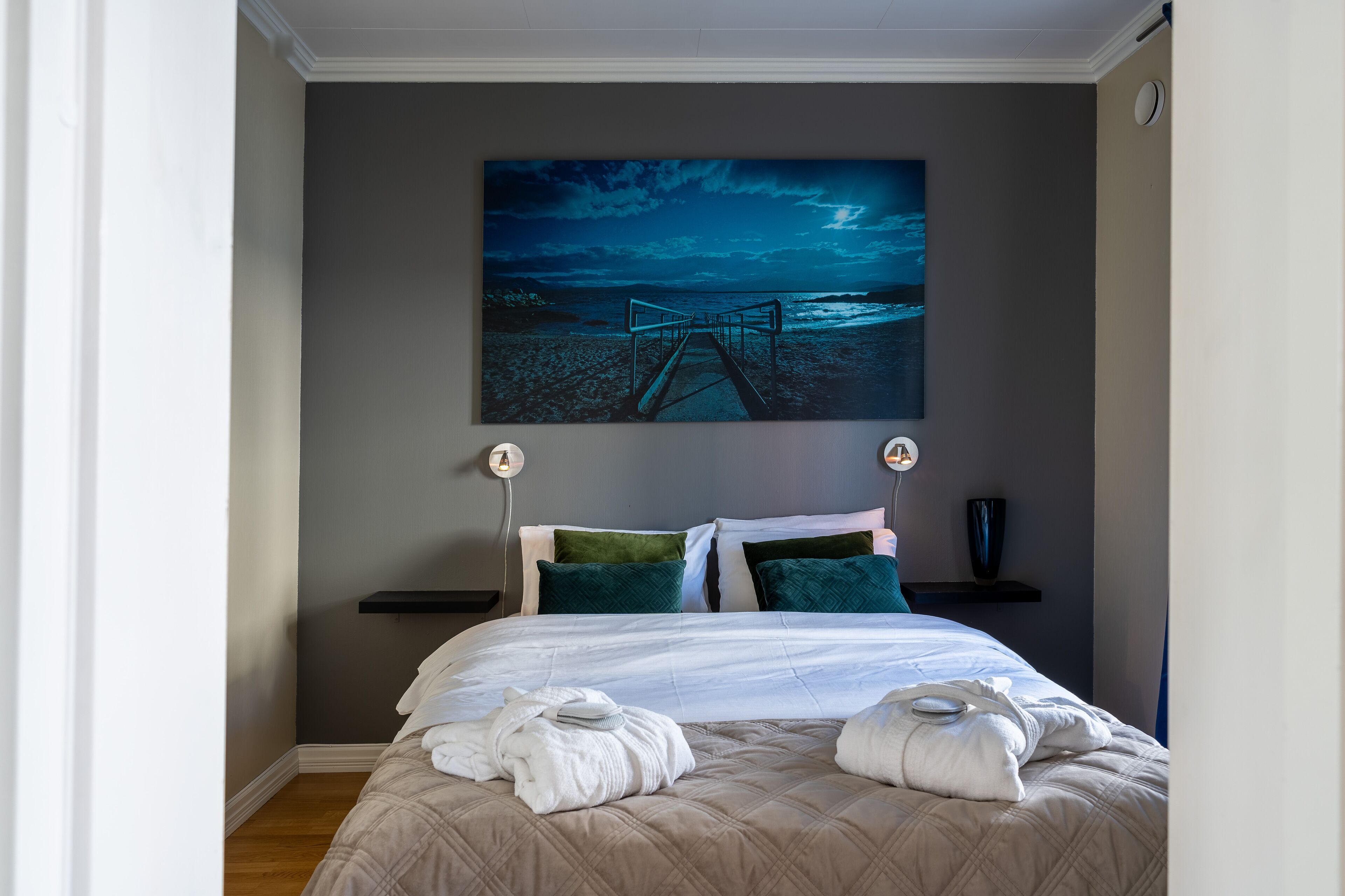 Un lit bien fait, recouvert d’une couette beige, avec deux oreillers et deux serviettes posées sur un plancher en bois.