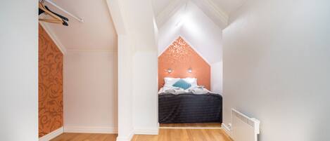 A bedroom with a sloped ceiling, a bed with white and blue bedding, a radiator, and a patterned wall.