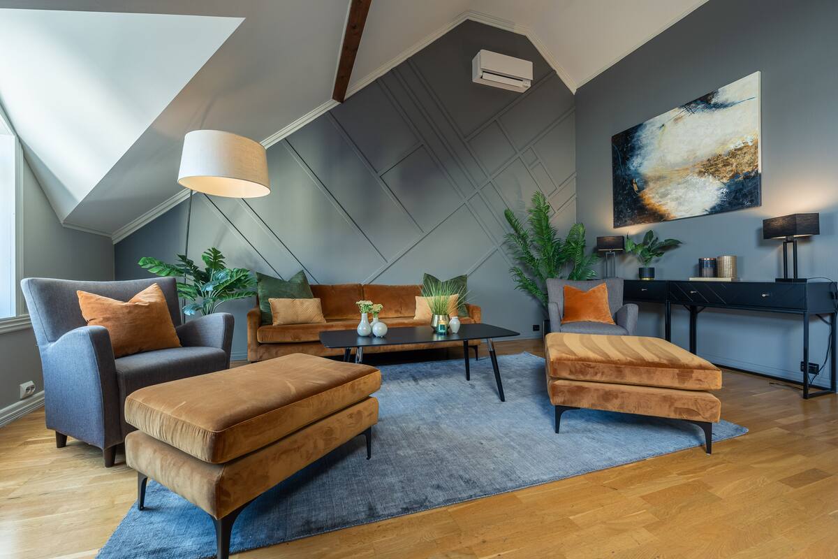 A modern living room with a loft-style ceiling, a large abstract painting, and a mix of furniture including a sofa, armchairs, and a coffee table.