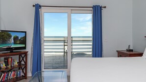 A bedroom with a bed, a TV on a wooden stand, a bookshelf, and a balcony with a view of the beach. - Gulf Front, Pet Friendly, N. Cape San Blas with Screened Deck ~ Whataday (Cape San Blas)