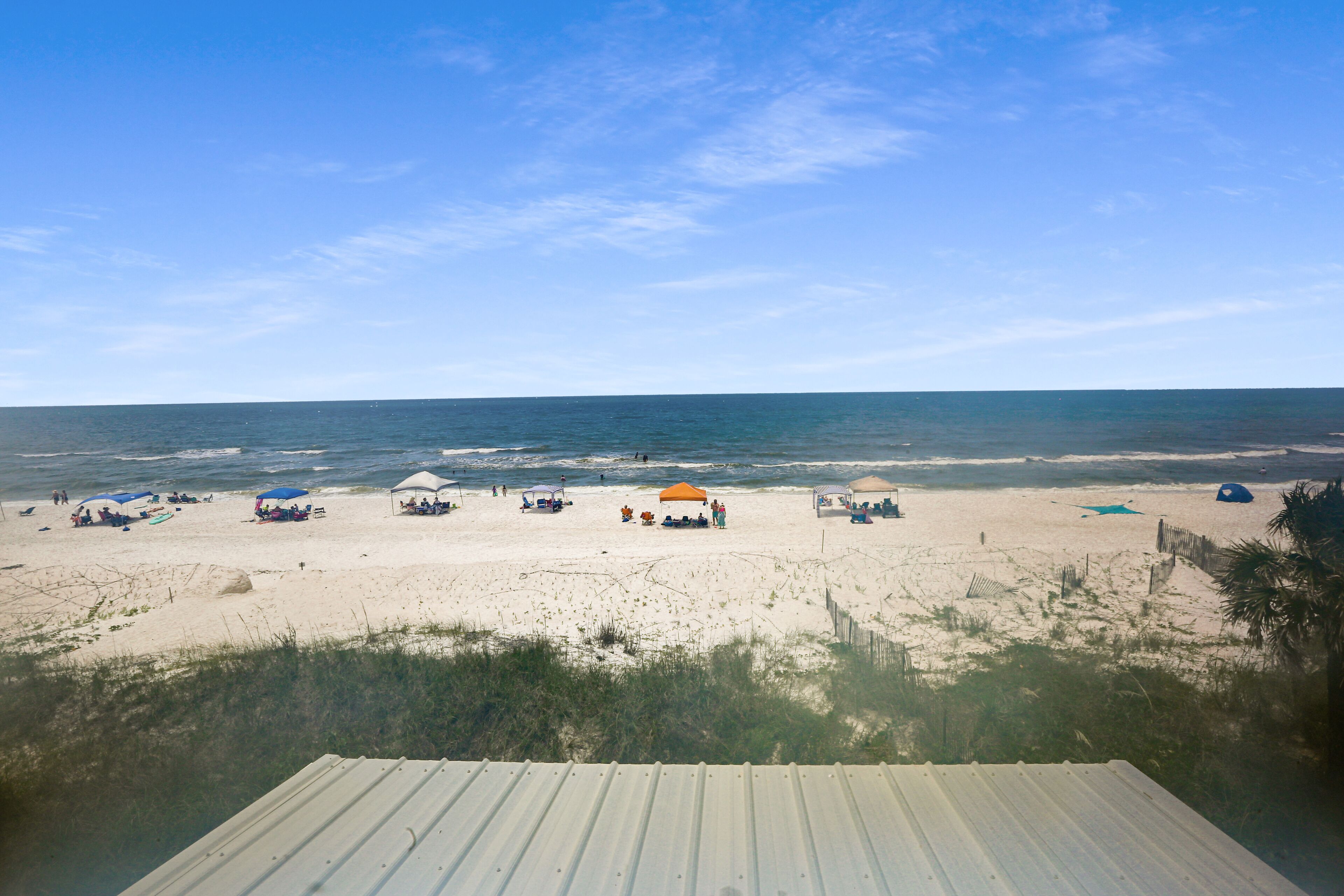 Uma praia com vários guarda-sóis e cadeiras de praia, uma faixa de areia e o oceano ao fundo.