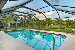 A swimming pool with a glass ceiling, surrounded by palm trees and a view of a house. - Waterfront Port St Lucie Home w/ Lanai & Pool (Port Saint Lucie)