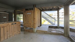 A covered outdoor area with a wooden trash bin labeled "Trash," a concrete floor, and a wooden staircase leading to an upper level. - Barrier Dunes, Close to Beach (Cape San Blas)