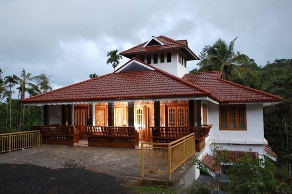 Traditional house with a red-tiled roof, porch, and lush surroundings.