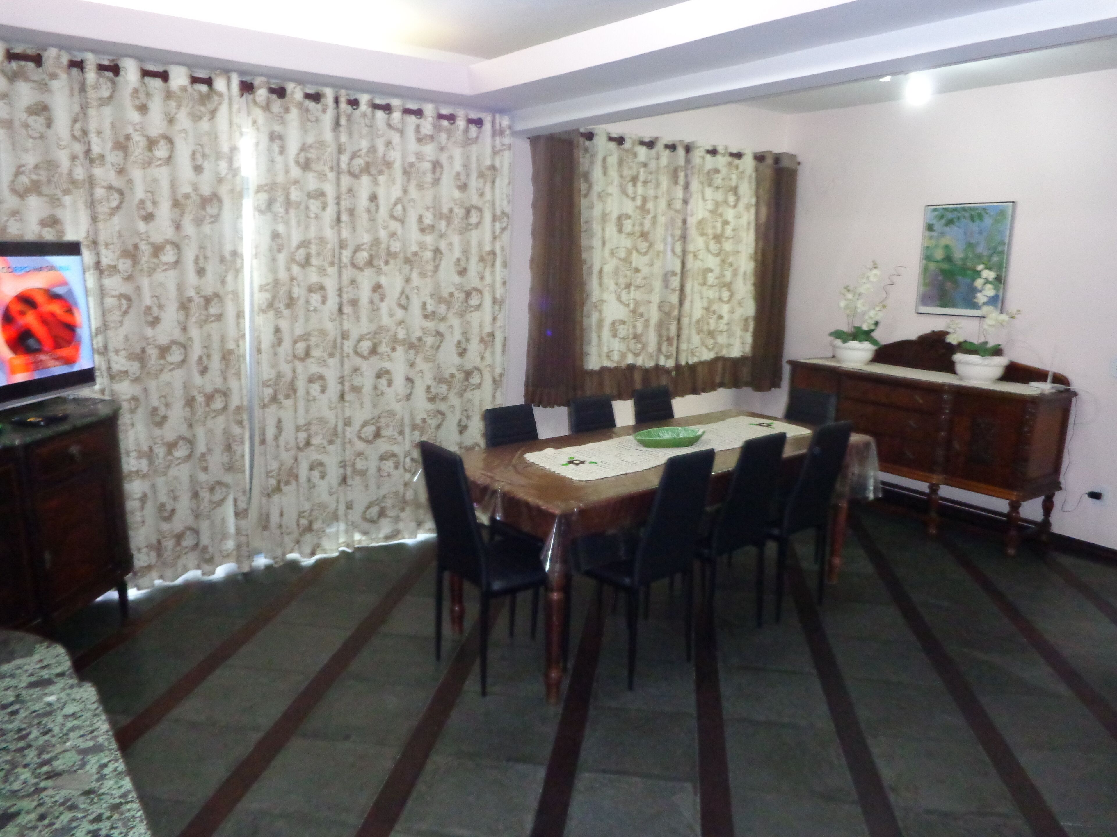 Un comedor con una mesa de madera, sillas negras, un tazón verde y un televisor sobre un mueble.