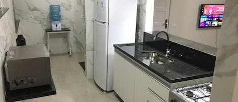 A compact kitchen with a refrigerator, sink, stove, and a water dispenser.