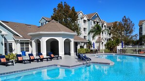 A swimming pool with lounge chairs and a covered seating area, surrounded by multi-story buildings with balconies.