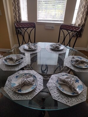 Enjoy meals in this dining area with a round table and six chairs, set with plates and a central napkin holder.