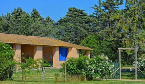 A single-story building with a tiled roof, surrounded by a fenced area with flowering bushes.