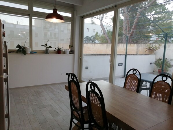 A dining area with a wooden table and four chairs, large windows, and potted plants on a balcony.