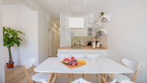 Una cocina moderna con armarios blancos, una isla central y una zona de comedor con mesa y sillas blancas.