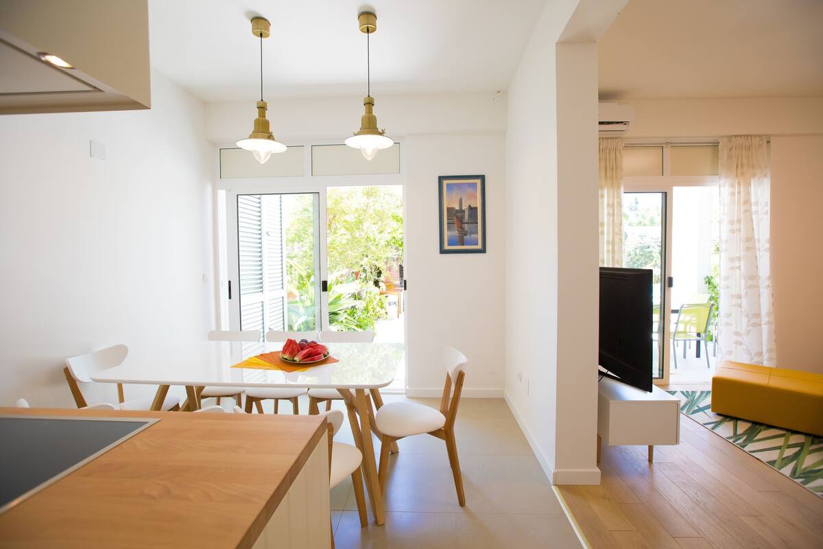 A modern kitchen with a dining table, chairs, and a TV.