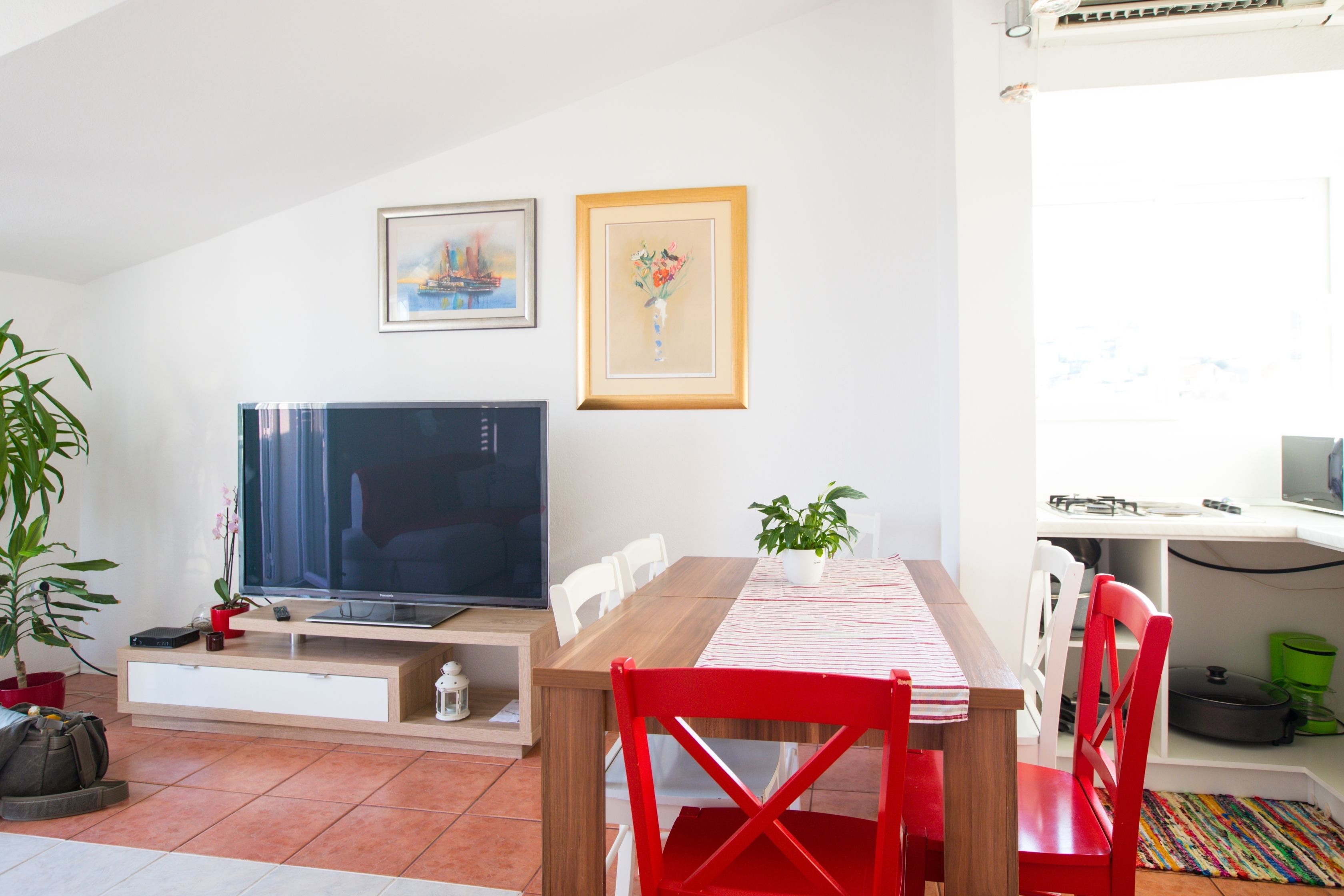 Ein modernes Wohnzimmer mit Flachbildfernseher, einem Esstisch mit Stühlen und einer Zimmerpflanze.