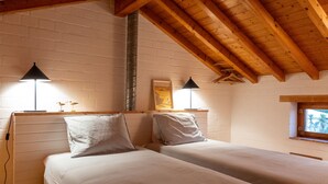 Ein Zimmer mit zwei Betten, Holzbalken, einer Backsteinwand und einem Fenster mit Blick.