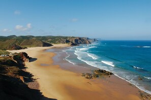 A coastal landscape with a sandy beach, ocean waves, and rocky cliffs.