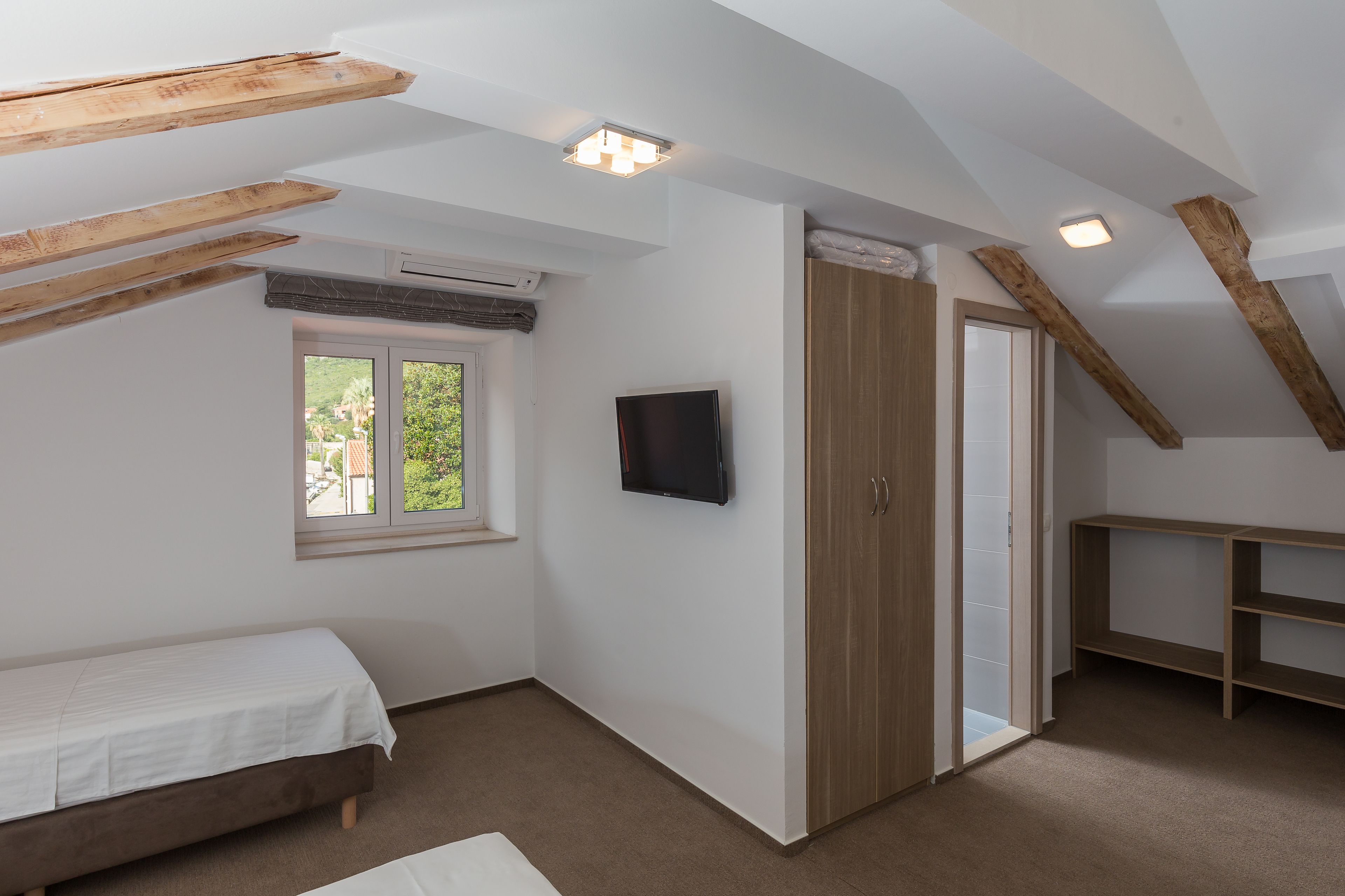 A bedroom with a bed, a TV, a wardrobe, and a window.