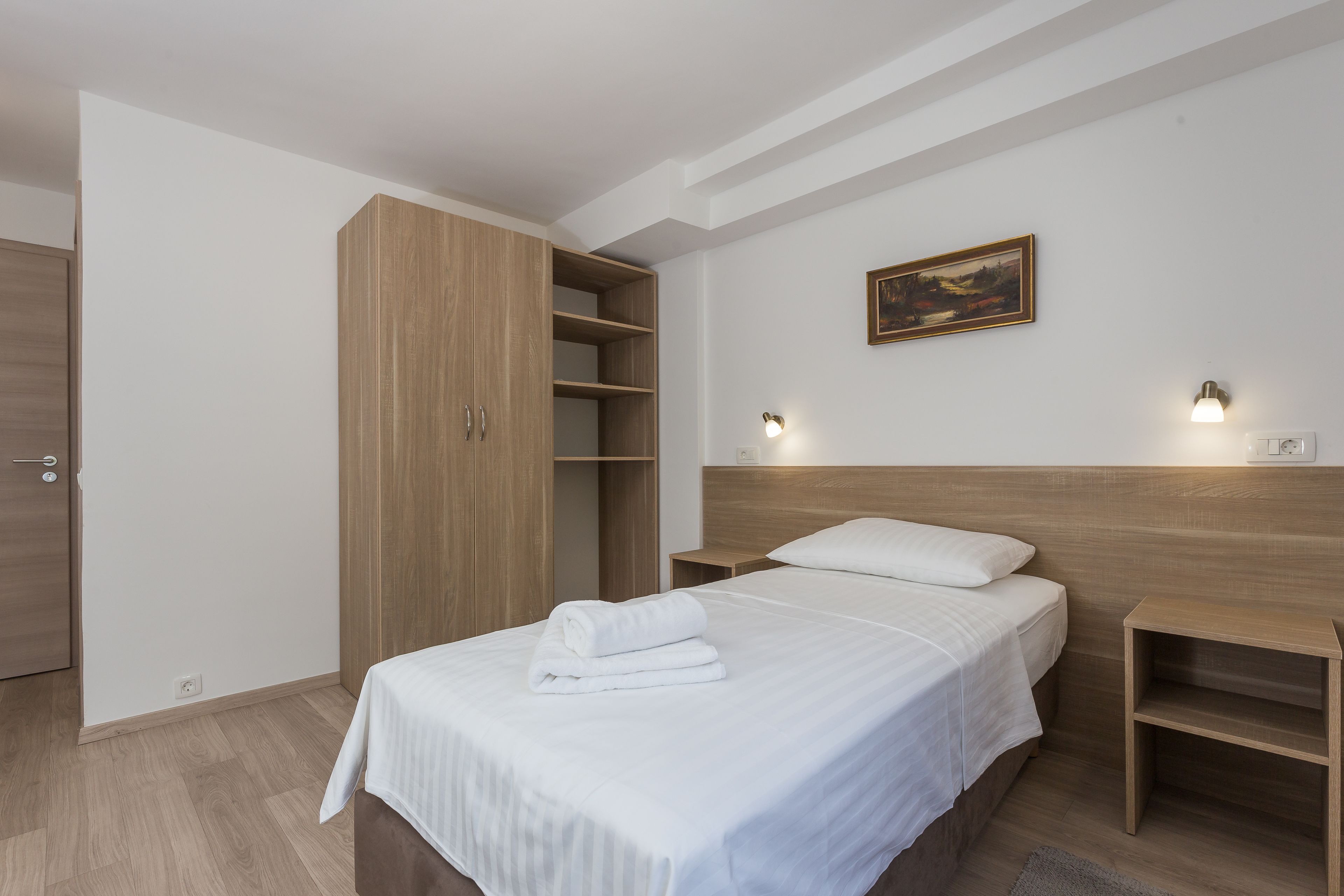 A bedroom with a bed, wooden wardrobe, bedside tables, and a painting on the wall.