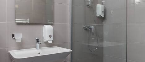 Un baño moderno con cabina de ducha de vidrio, un lavabo con dispensador de jabón y un espejo.