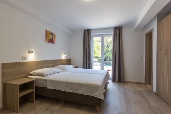 Un dormitorio con cama doble, mesita de noche, un cuadro en la pared y ventana con cortinas.