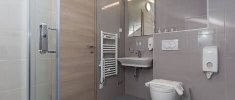 Ein modernes Badezimmer mit einer Duschkabine aus Glas, einer Holztür, einem weißen Waschbecken, einer Toilette und einem Spiegel mit Beleuchtung darüber.