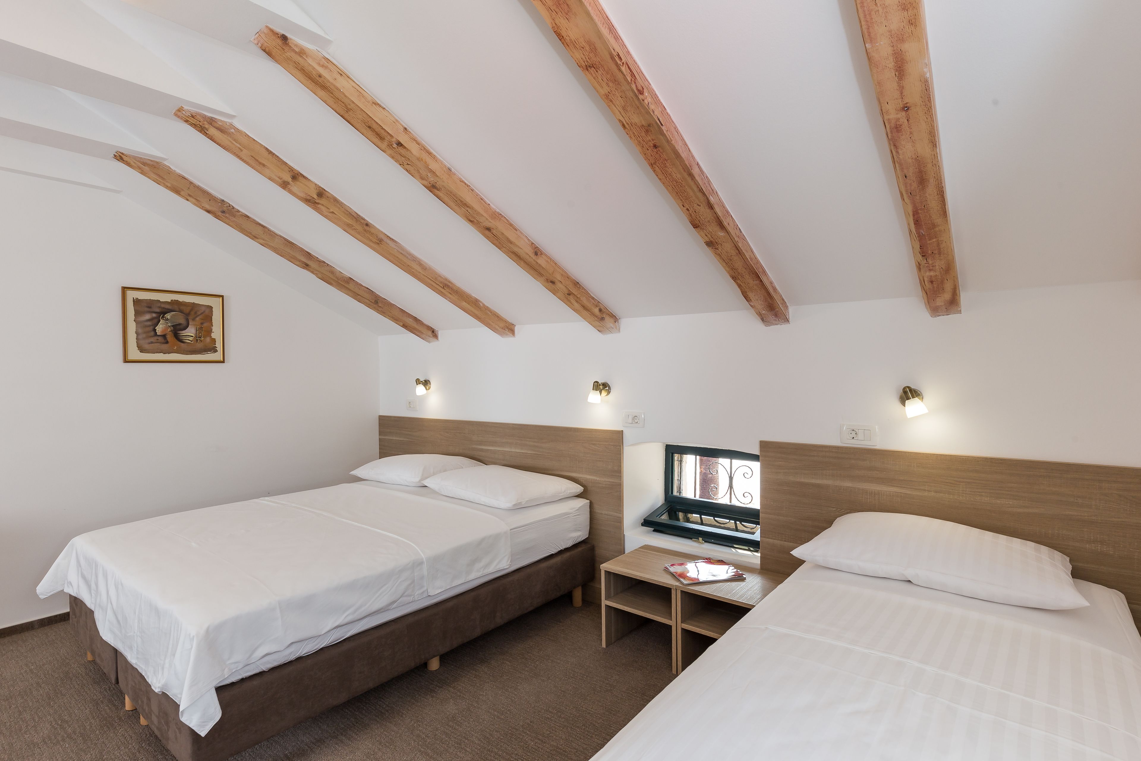 Une chambre avec deux lits, des poutres en bois au plafond, une petite table de chevet et un luminaire fixé au mur.
